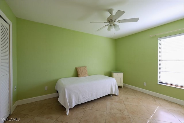 bedroom featuring multiple windows, light tile patterned flooring, ceiling fan, and a closet