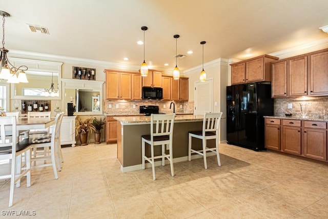 kitchen with pendant lighting, a breakfast bar area, a kitchen island with sink, light stone counters, and black appliances