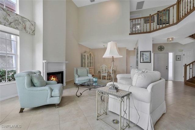 living area with a warm lit fireplace, light tile patterned flooring, a high ceiling, visible vents, and stairway