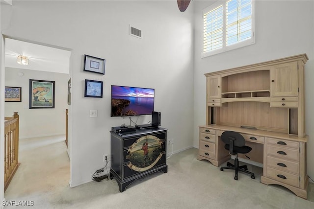 office featuring baseboards, a high ceiling, visible vents, and light colored carpet