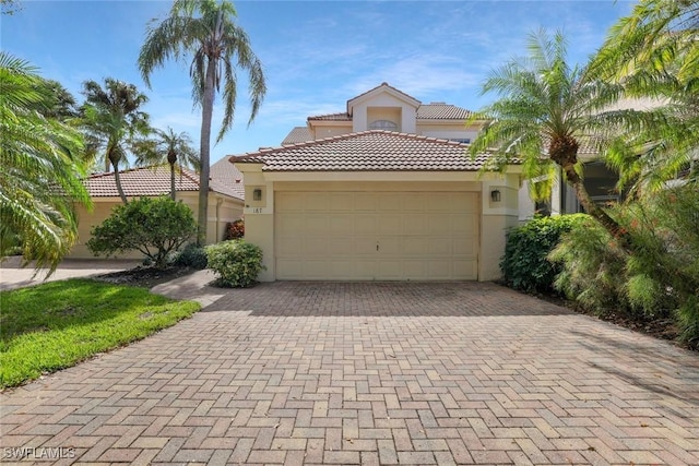 mediterranean / spanish-style home with a garage, decorative driveway, a tile roof, and stucco siding