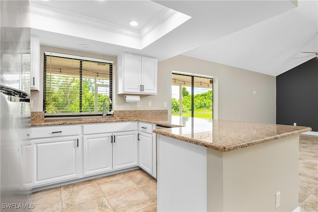 kitchen with a healthy amount of sunlight, white cabinets, light stone counters, and kitchen peninsula