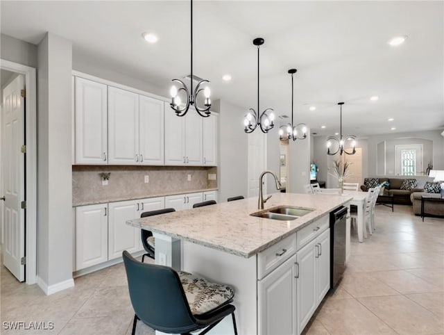 kitchen with pendant lighting, white cabinetry, sink, light stone counters, and a center island with sink