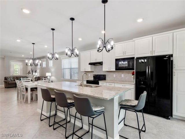 kitchen with pendant lighting, black appliances, white cabinets, and a center island with sink