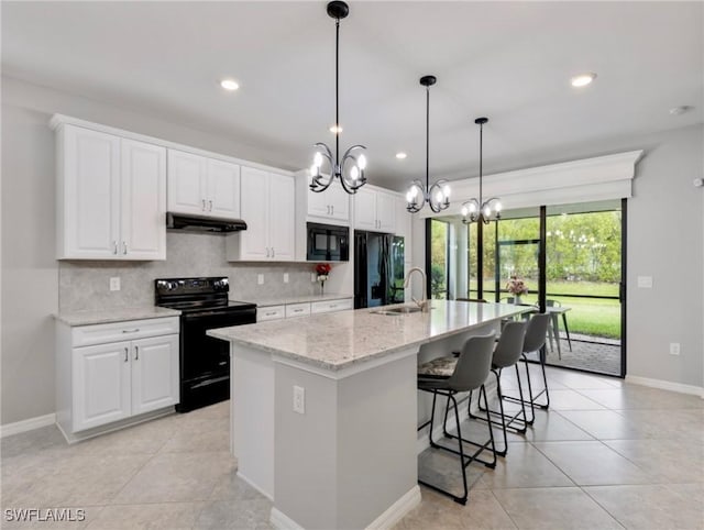 kitchen with white cabinets, backsplash, black appliances, light stone countertops, and a center island with sink