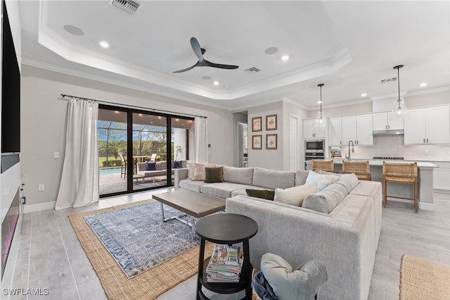 living room featuring sink, a tray ceiling, ornamental molding, and ceiling fan