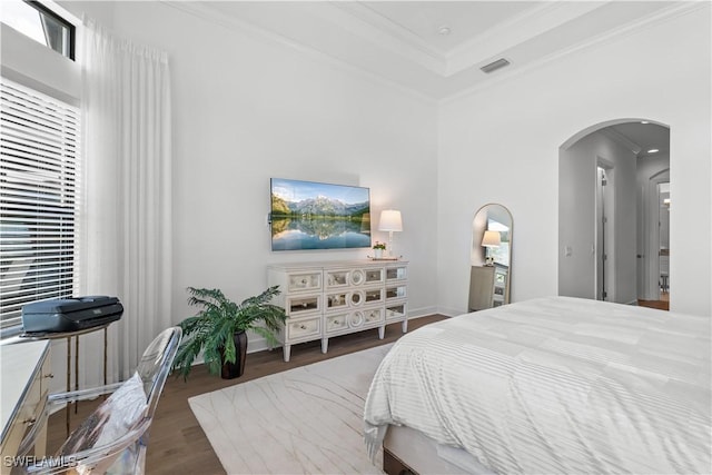 bedroom with arched walkways, a tray ceiling, crown molding, visible vents, and wood finished floors