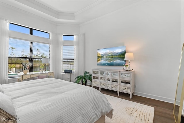 bedroom featuring baseboards, a raised ceiling, wood finished floors, and crown molding