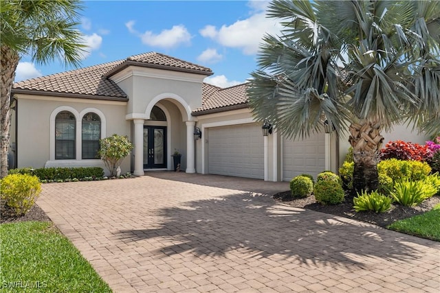 mediterranean / spanish-style house featuring stucco siding, french doors, a garage, a tiled roof, and decorative driveway