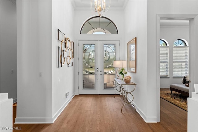 interior space with a notable chandelier, wood finished floors, baseboards, french doors, and ornamental molding