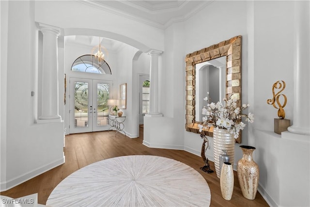 entrance foyer with arched walkways, wood finished floors, french doors, ornamental molding, and ornate columns