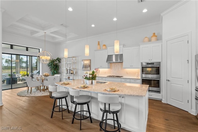 kitchen with dark wood-style flooring, coffered ceiling, backsplash, and under cabinet range hood