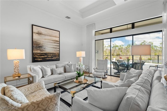 living room with a tray ceiling, wood finished floors, visible vents, and crown molding