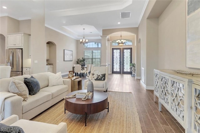 living area with arched walkways, a notable chandelier, wood finished floors, visible vents, and crown molding