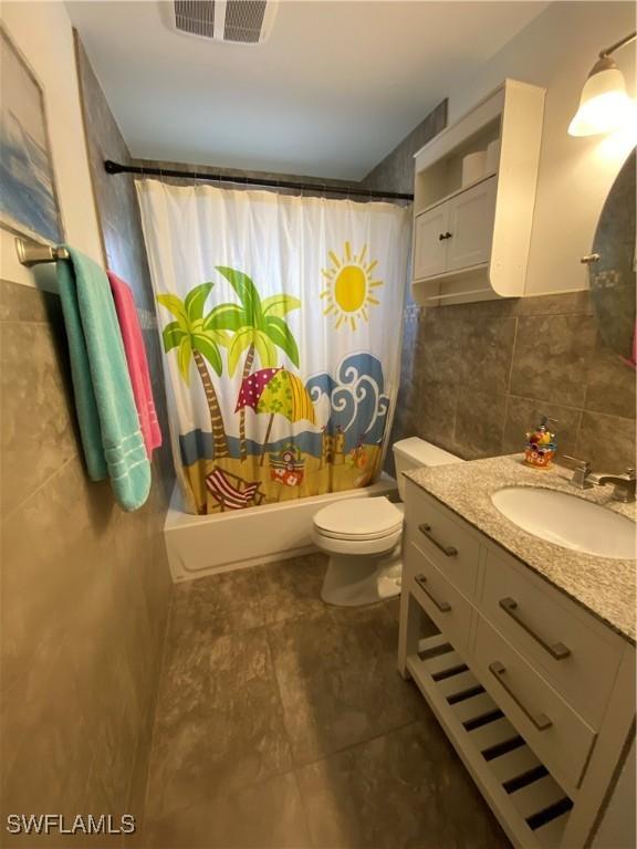 full bathroom with visible vents, toilet, shower / bath combo with shower curtain, vanity, and tile walls