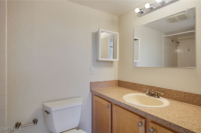 bathroom with tiled shower, vanity, and toilet