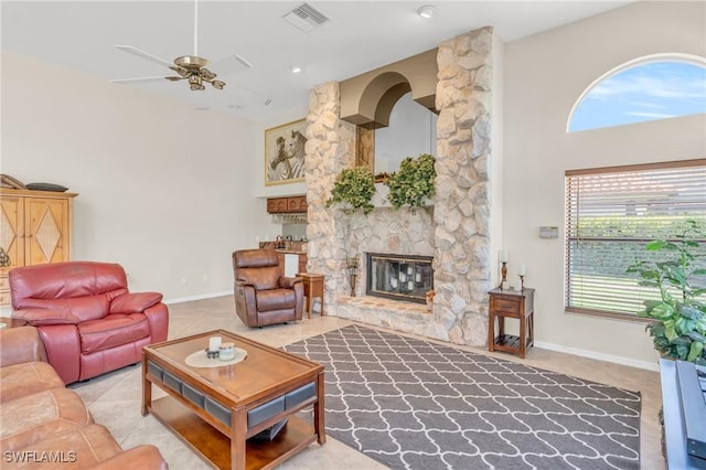 living room featuring light tile patterned flooring, a stone fireplace, a towering ceiling, and ceiling fan