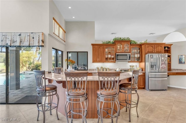 kitchen with light stone countertops, light tile patterned floors, stainless steel appliances, and a kitchen breakfast bar