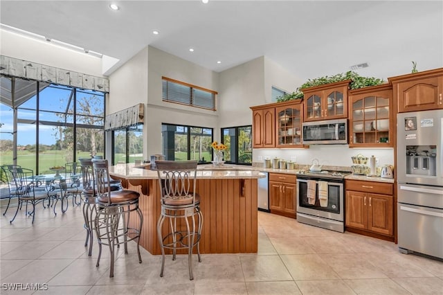 kitchen with a kitchen island, appliances with stainless steel finishes, a towering ceiling, and a breakfast bar