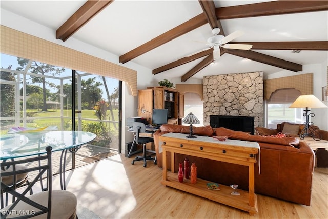 living room featuring vaulted ceiling with beams, a wealth of natural light, a fireplace, and light hardwood / wood-style floors