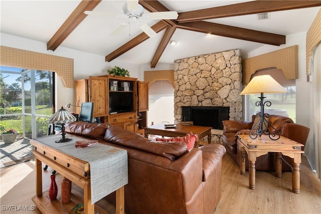 living room featuring ceiling fan, a stone fireplace, vaulted ceiling with beams, and light hardwood / wood-style floors