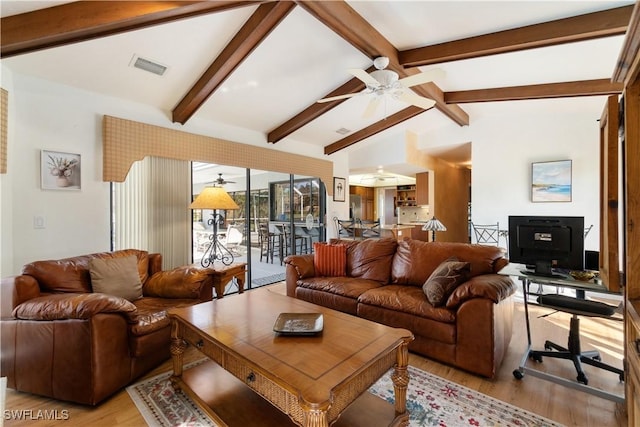 living room featuring vaulted ceiling with beams, a wood stove, ceiling fan, and light wood-type flooring