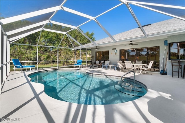 view of swimming pool featuring a bar, ceiling fan, glass enclosure, and a patio area