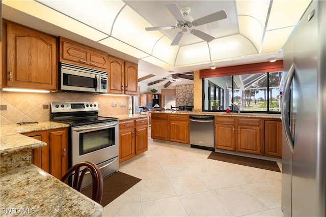 kitchen with light stone counters, stainless steel appliances, a raised ceiling, and backsplash