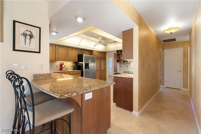 kitchen featuring stainless steel refrigerator with ice dispenser, a kitchen bar, light stone counters, kitchen peninsula, and a raised ceiling