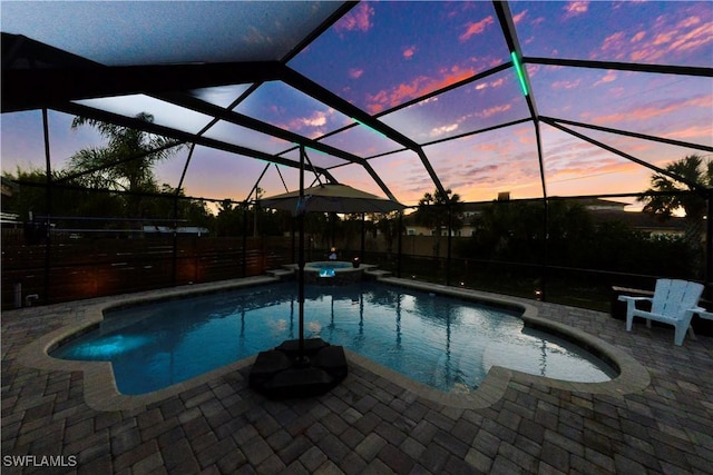 pool at dusk featuring a patio area, an in ground hot tub, and glass enclosure