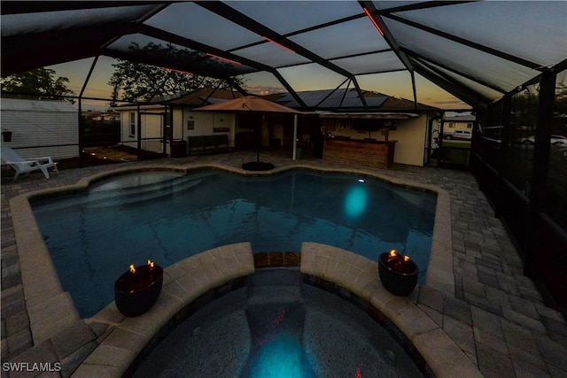 pool at dusk featuring an in ground hot tub, a lanai, and a patio area