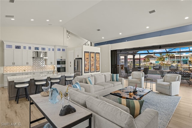 living room with high vaulted ceiling, light hardwood / wood-style floors, and sink