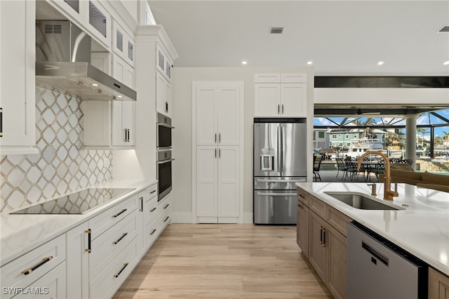 kitchen featuring white cabinetry, sink, wall chimney range hood, and appliances with stainless steel finishes