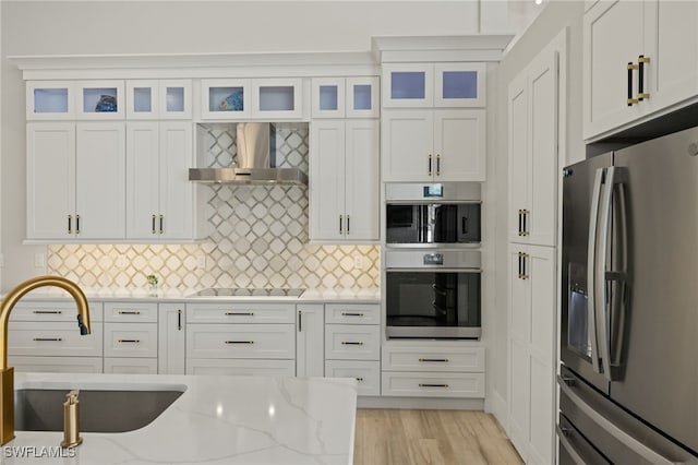 kitchen featuring sink, appliances with stainless steel finishes, white cabinetry, light stone counters, and wall chimney exhaust hood