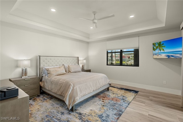 bedroom with light hardwood / wood-style flooring, a raised ceiling, and ceiling fan