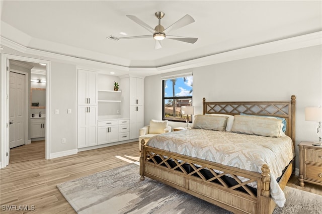 bedroom featuring a tray ceiling, connected bathroom, ceiling fan, and light hardwood / wood-style flooring