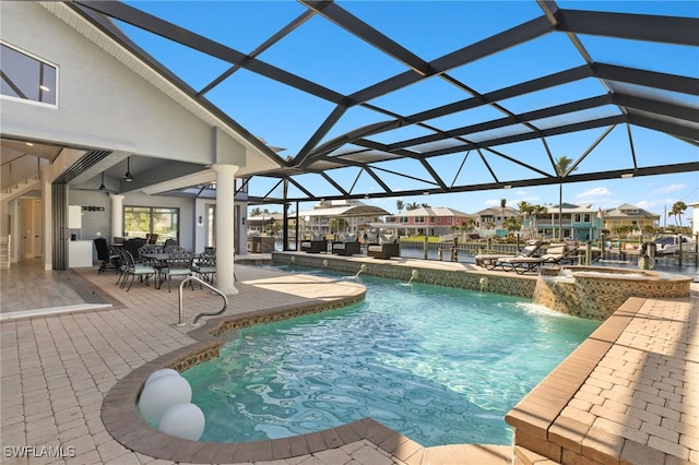 view of pool with an in ground hot tub, a water view, a patio, and glass enclosure