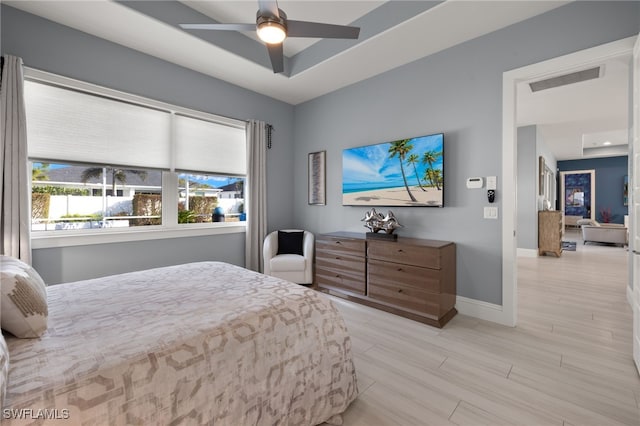 bedroom with ceiling fan, a raised ceiling, and light hardwood / wood-style flooring