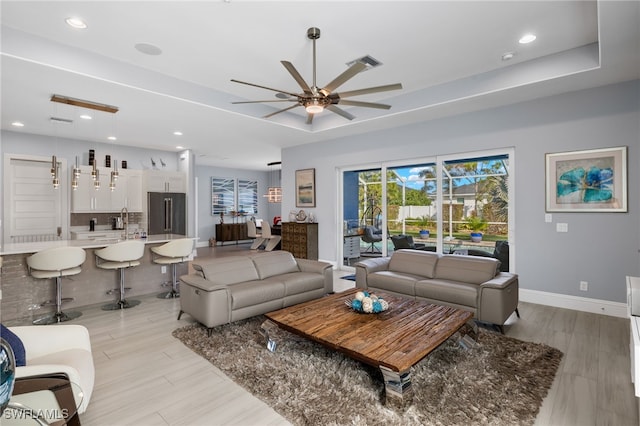 living room featuring a raised ceiling, ceiling fan, and light wood-type flooring