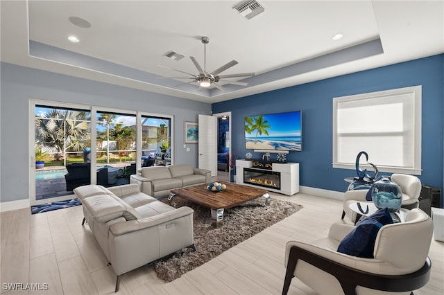 living room featuring light hardwood / wood-style flooring, a raised ceiling, and ceiling fan