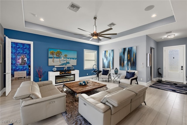 living room featuring ceiling fan, a raised ceiling, and light hardwood / wood-style floors