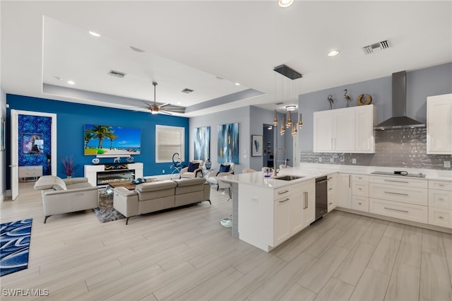 kitchen featuring wall chimney range hood, sink, black electric stovetop, a tray ceiling, and white cabinets