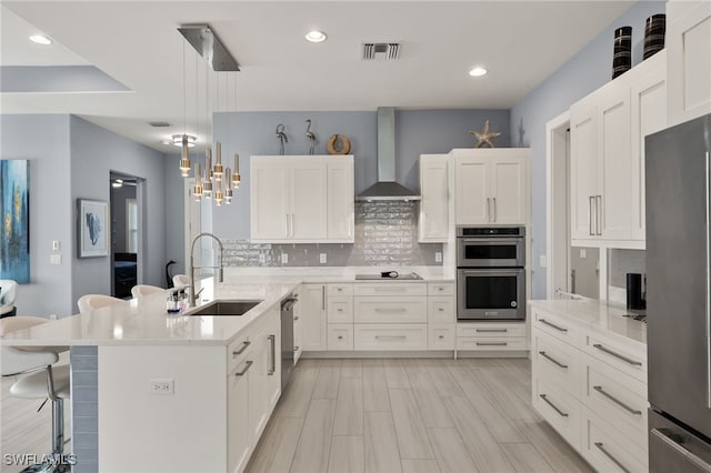 kitchen featuring wall chimney exhaust hood, a breakfast bar, sink, decorative light fixtures, and appliances with stainless steel finishes