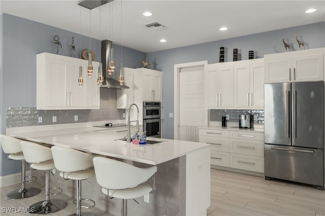 kitchen featuring white cabinets, decorative light fixtures, wall chimney exhaust hood, and appliances with stainless steel finishes