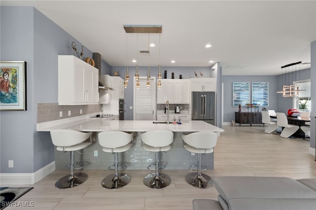 kitchen with white cabinetry, decorative light fixtures, a kitchen breakfast bar, kitchen peninsula, and stainless steel appliances