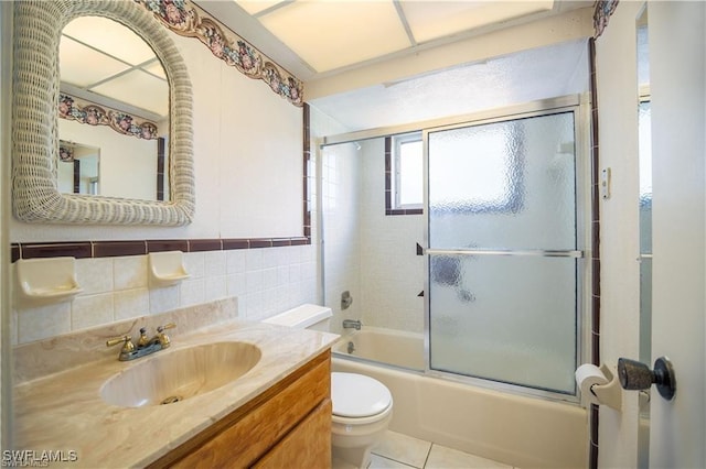 full bathroom with shower / bath combination with glass door, tile walls, tile patterned flooring, vanity, and toilet