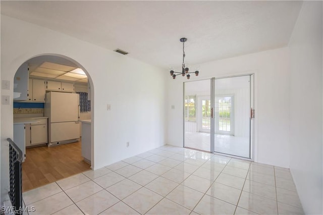 tiled spare room featuring a notable chandelier