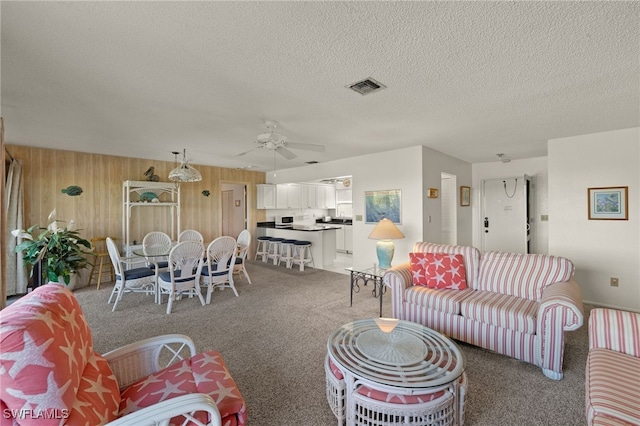 carpeted living room featuring a textured ceiling, ceiling fan, and wood walls