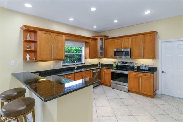 kitchen with sink, a kitchen breakfast bar, dark stone counters, stainless steel appliances, and kitchen peninsula