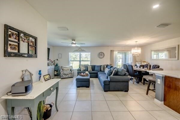 tiled living room with ceiling fan with notable chandelier